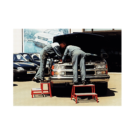 Zwei Mechaniker reparieren einen Transporter unter der geöffneten Motorhaube. Sie stehen auf roten Trittschemeln.